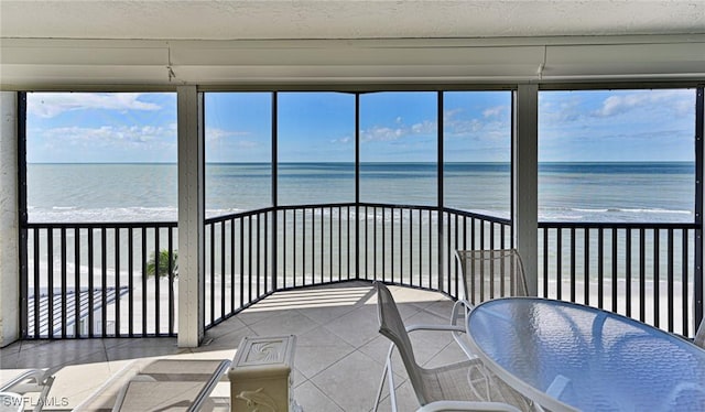 sunroom featuring a beach view and a water view