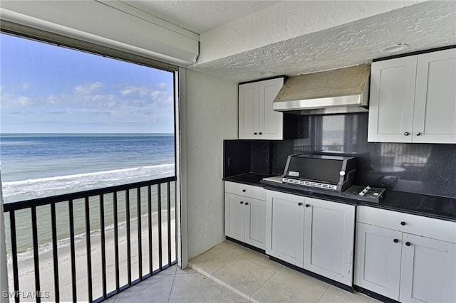 kitchen with a water view, white cabinets, wall chimney range hood, light tile patterned flooring, and tasteful backsplash