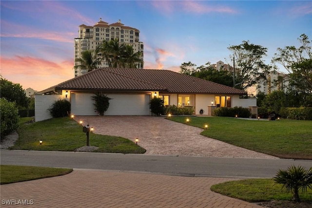 view of front of home featuring a tiled roof, stucco siding, decorative driveway, a garage, and a yard