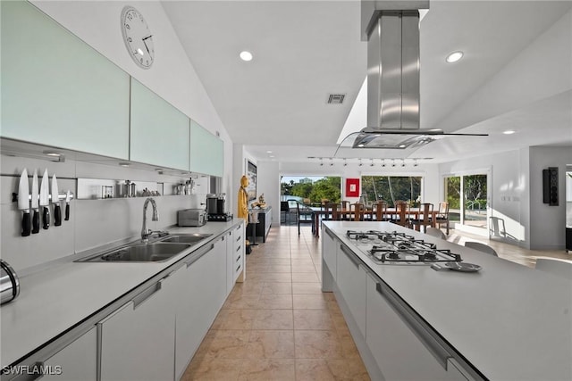 kitchen featuring sink, tasteful backsplash, island range hood, stainless steel gas cooktop, and white cabinets