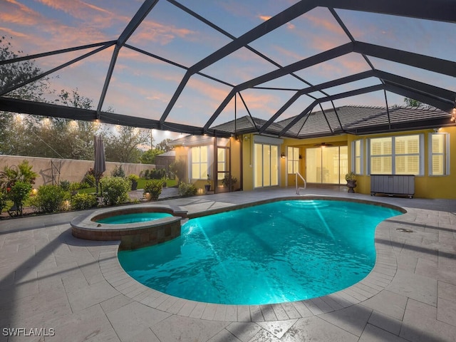 pool at dusk featuring a patio, glass enclosure, and an in ground hot tub