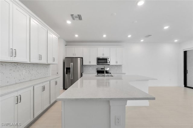 kitchen with appliances with stainless steel finishes, a kitchen island with sink, white cabinets, and light stone counters