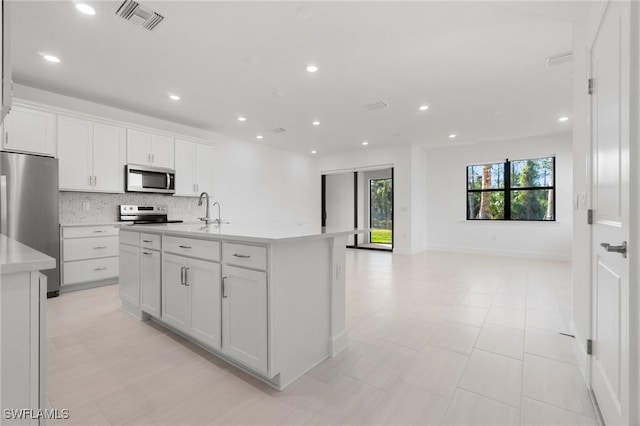 kitchen featuring stainless steel appliances, a kitchen island with sink, white cabinets, and backsplash