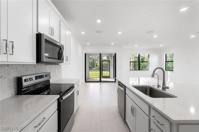 kitchen with white cabinetry, sink, backsplash, light stone counters, and stainless steel appliances