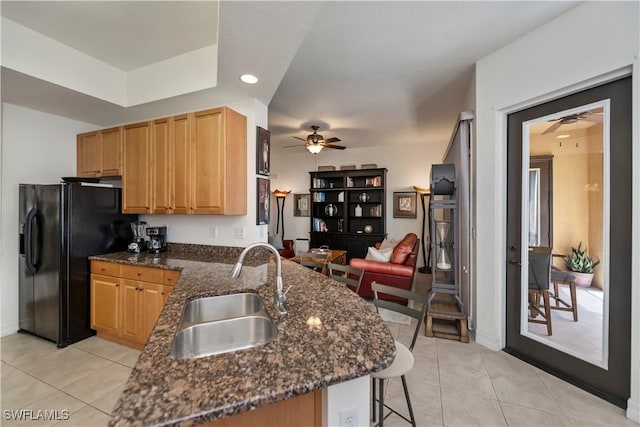 kitchen with black fridge, kitchen peninsula, sink, and dark stone counters