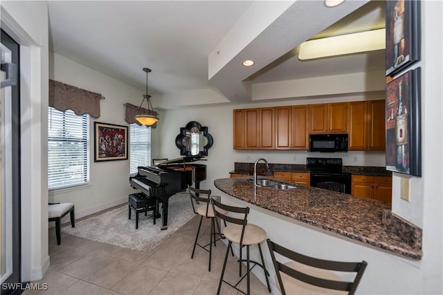 kitchen with sink, dark stone countertops, decorative light fixtures, a kitchen bar, and black appliances