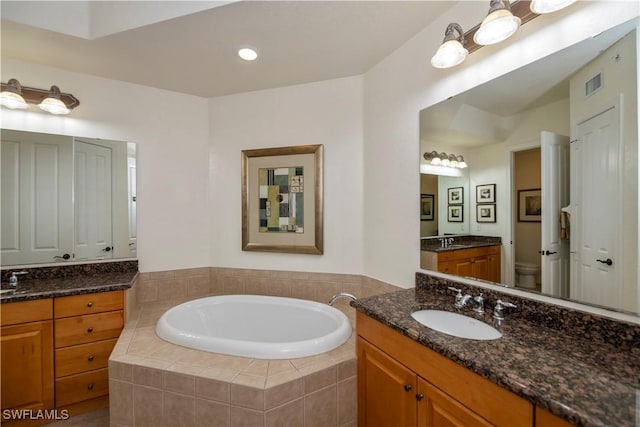 bathroom with tiled tub, vanity, and toilet