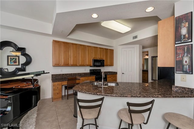 kitchen with sink, kitchen peninsula, dark stone countertops, a breakfast bar, and black appliances