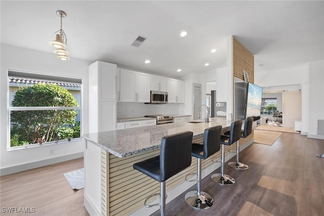 kitchen with light stone countertops, stainless steel appliances, decorative light fixtures, a kitchen bar, and white cabinets