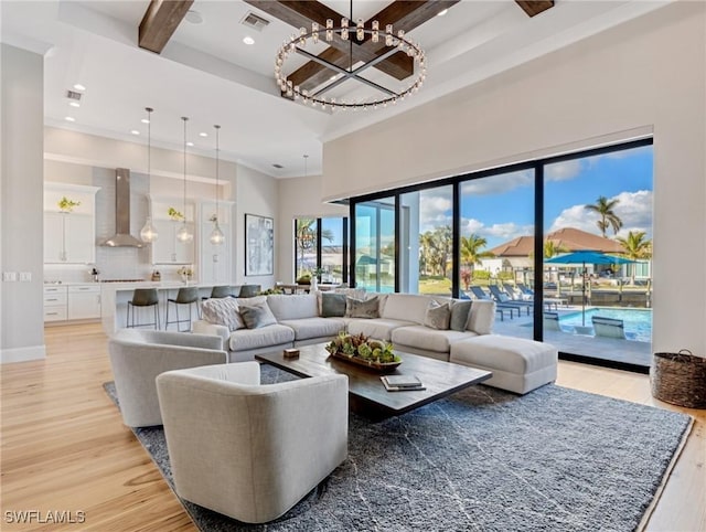 living room featuring a towering ceiling, an inviting chandelier, light hardwood / wood-style floors, and beamed ceiling