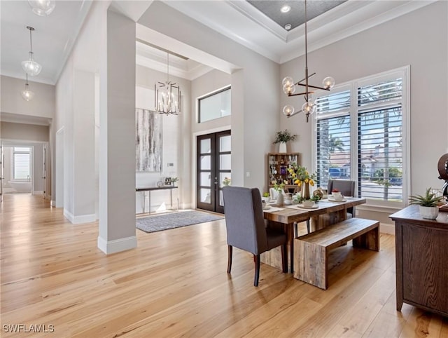 dining room featuring light hardwood / wood-style flooring, a chandelier, french doors, a tray ceiling, and crown molding