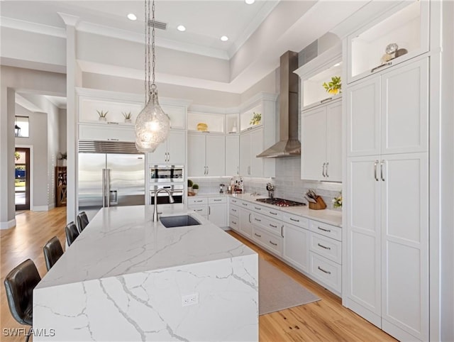 kitchen featuring built in appliances, wall chimney exhaust hood, pendant lighting, an island with sink, and sink