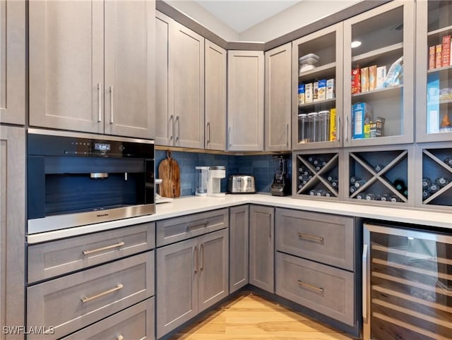 bar with light hardwood / wood-style flooring, tasteful backsplash, oven, beverage cooler, and gray cabinetry