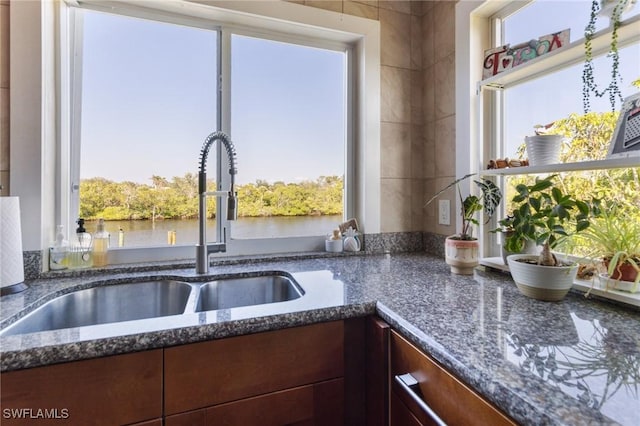 kitchen featuring sink, dark stone counters, and a water view