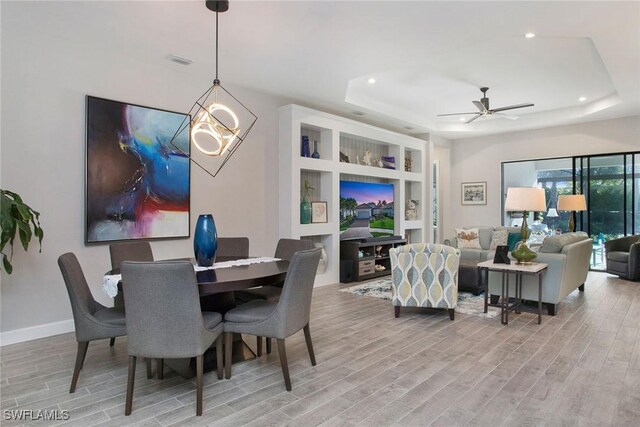 dining room featuring light hardwood / wood-style floors, built in features, a raised ceiling, and ceiling fan with notable chandelier