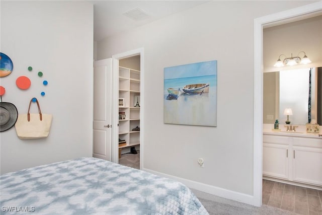 bedroom with visible vents, baseboards, a sink, ensuite bathroom, and a walk in closet