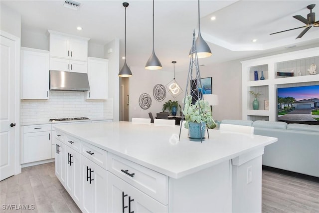 kitchen featuring under cabinet range hood, visible vents, open floor plan, and light wood-style flooring