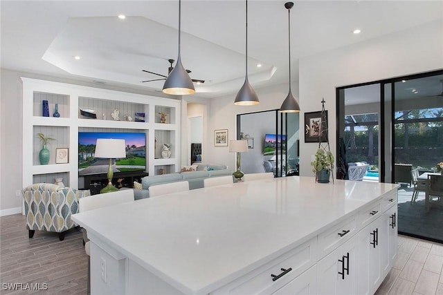 kitchen featuring wood finish floors, pendant lighting, a tray ceiling, recessed lighting, and white cabinets