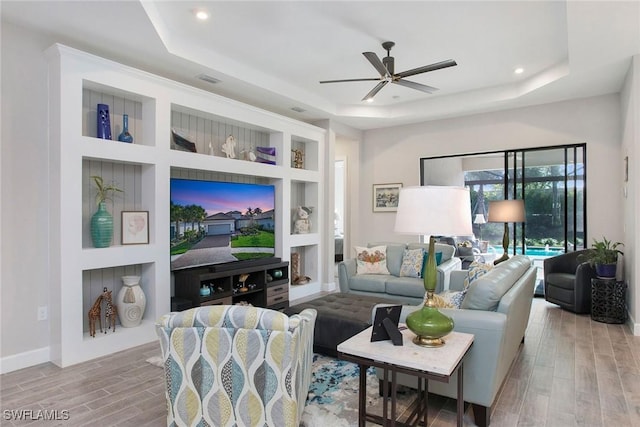 living area featuring built in shelves, wood tiled floor, recessed lighting, ceiling fan, and a raised ceiling