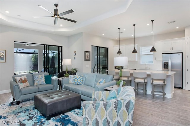 living area with visible vents, light wood-style flooring, recessed lighting, a raised ceiling, and ceiling fan