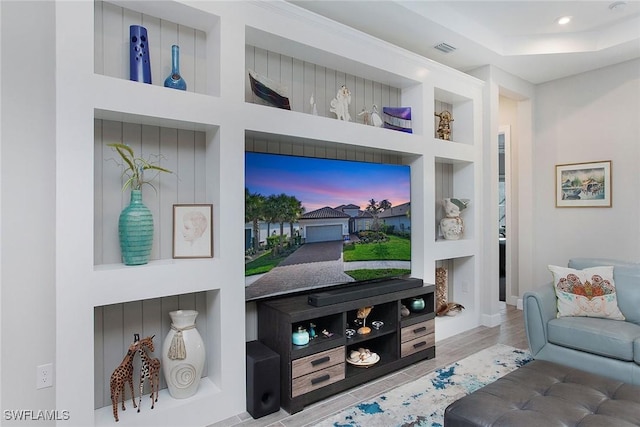 living area featuring visible vents, built in shelves, a raised ceiling, and wood finished floors