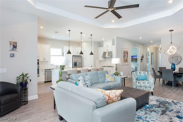 living area featuring a raised ceiling, light wood-style flooring, and recessed lighting