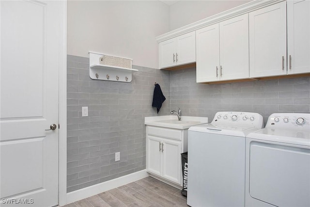 washroom with a sink, washing machine and dryer, cabinet space, light wood-style floors, and tile walls