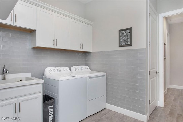 clothes washing area with light wood-type flooring, a sink, cabinet space, tile walls, and washing machine and clothes dryer