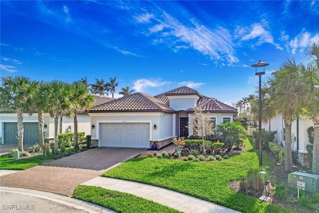 mediterranean / spanish-style home with stucco siding, a front lawn, a garage, stone siding, and decorative driveway