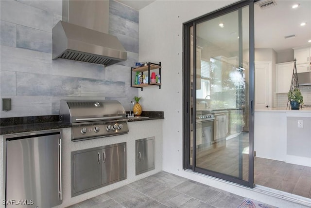 kitchen with visible vents, backsplash, refrigerator, white cabinetry, and wall chimney range hood