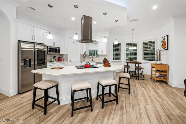 kitchen featuring a kitchen bar, island exhaust hood, white cabinetry, and appliances with stainless steel finishes