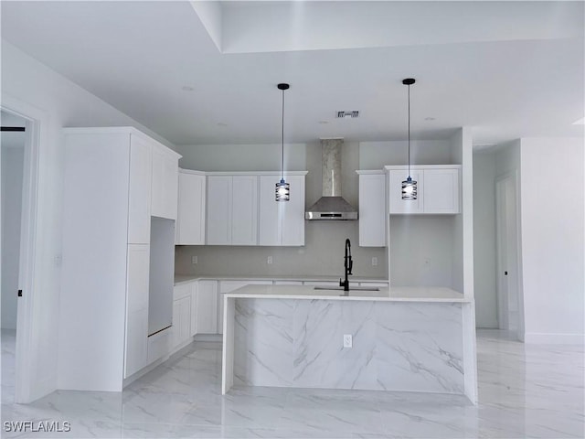 kitchen with white cabinets, sink, hanging light fixtures, wall chimney exhaust hood, and an island with sink