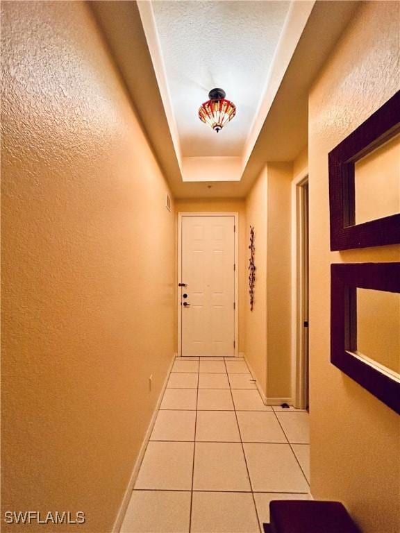 corridor featuring tile patterned flooring, a textured ceiling, and a raised ceiling