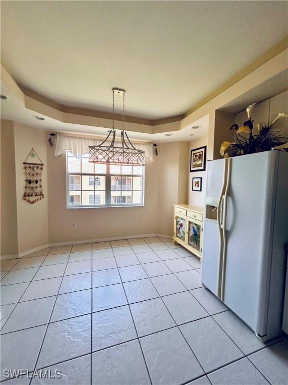 kitchen featuring white refrigerator with ice dispenser, light tile patterned floors, a raised ceiling, and hanging light fixtures