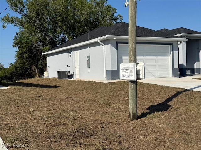 view of side of home with stucco siding, driveway, central AC, a yard, and an attached garage