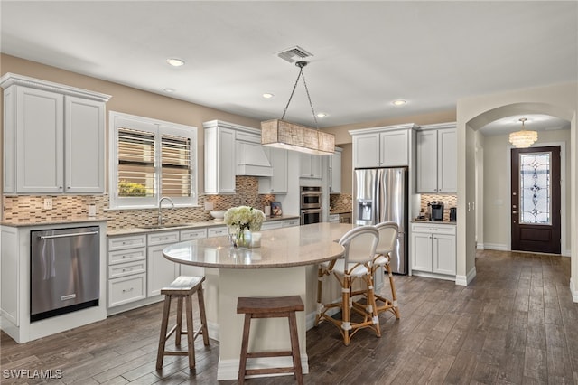 kitchen with stainless steel appliances, sink, white cabinets, a center island, and hanging light fixtures