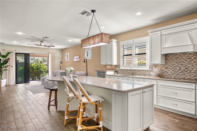 kitchen featuring black cooktop, pendant lighting, a breakfast bar, a kitchen island, and custom range hood