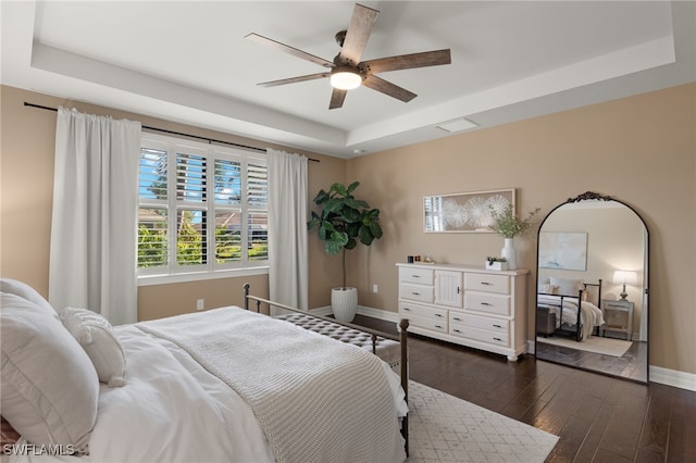 bedroom with ceiling fan, dark wood-type flooring, and a tray ceiling