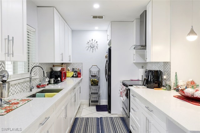 kitchen with wall chimney exhaust hood, sink, light tile patterned floors, decorative light fixtures, and white cabinets