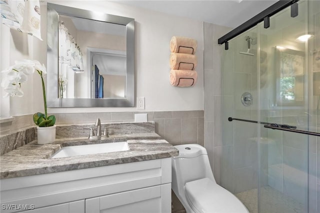 bathroom featuring vanity, a shower with door, toilet, and tile walls