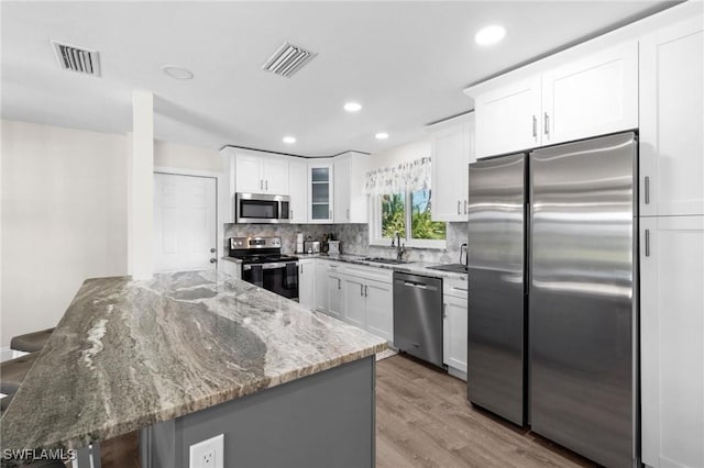 kitchen with kitchen peninsula, light stone counters, a breakfast bar, stainless steel appliances, and white cabinets