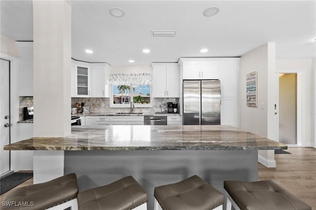 kitchen with a kitchen bar, light stone counters, stainless steel appliances, sink, and white cabinets