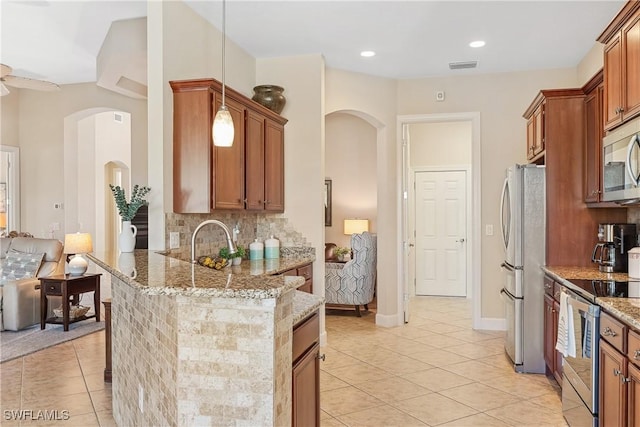 kitchen with appliances with stainless steel finishes, light tile patterned floors, tasteful backsplash, and light stone counters