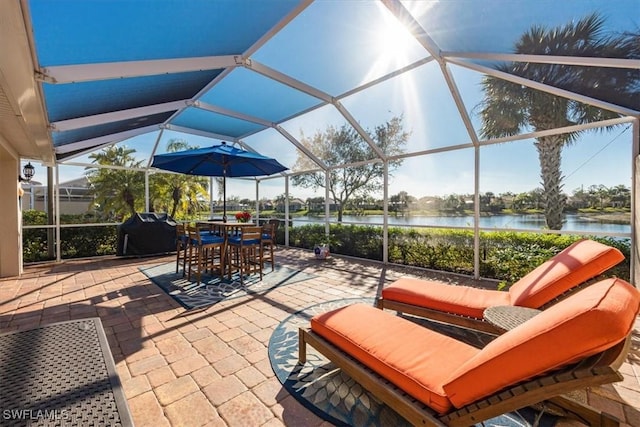 view of patio / terrace featuring glass enclosure, area for grilling, and a water view