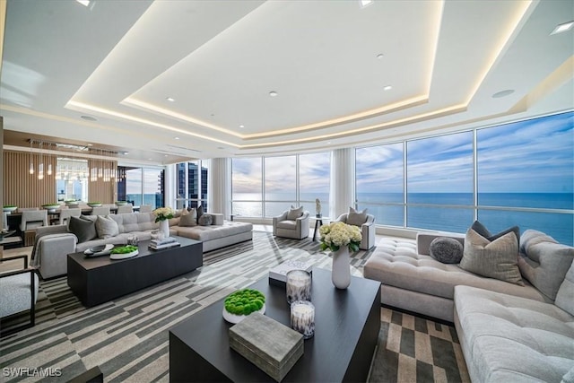 carpeted living room with a raised ceiling, expansive windows, a water view, and a wealth of natural light