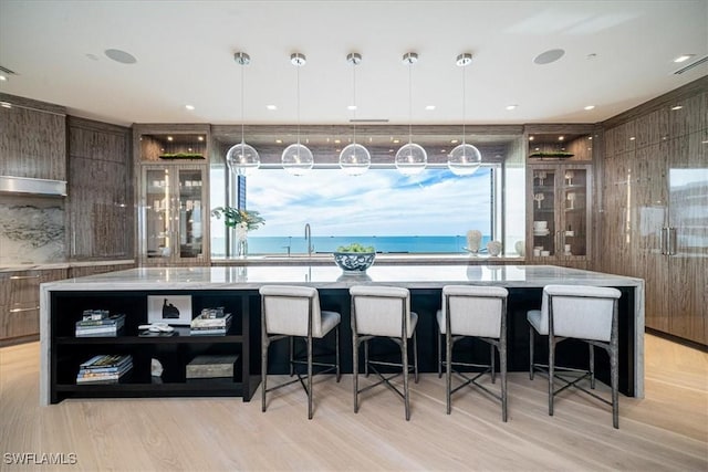 kitchen with hanging light fixtures, a water view, light hardwood / wood-style flooring, and a large island