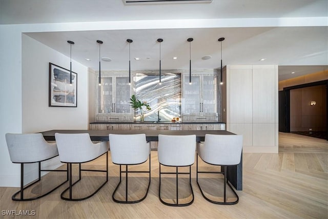 bar with light parquet floors, white cabinetry, and hanging light fixtures