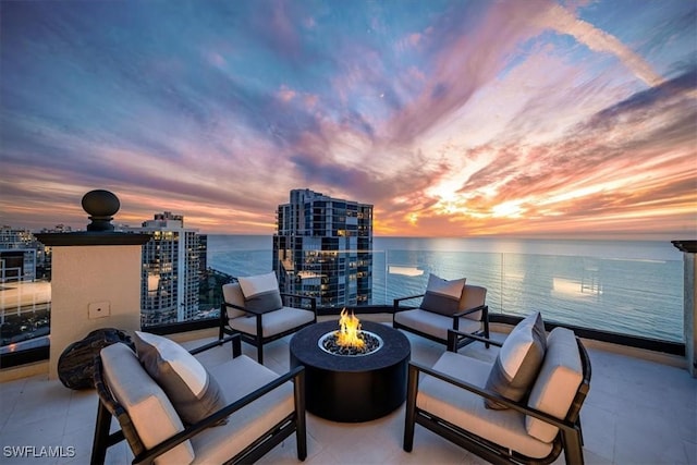 balcony at dusk featuring an outdoor living space with a fire pit and a water view