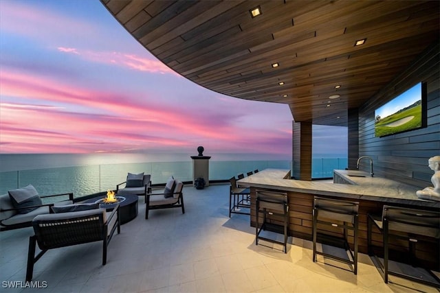 patio terrace at dusk with a water view, a wet bar, and an outdoor living space with a fire pit