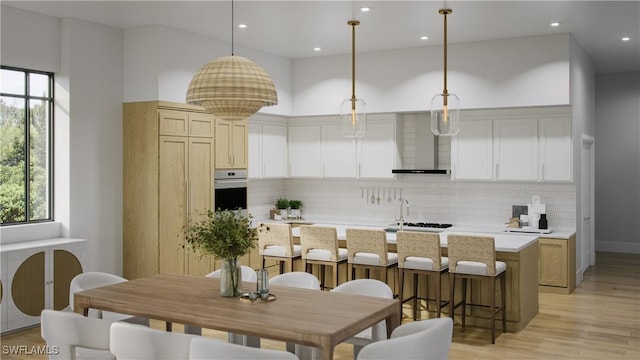 kitchen with decorative backsplash, wall chimney exhaust hood, pendant lighting, oven, and an island with sink